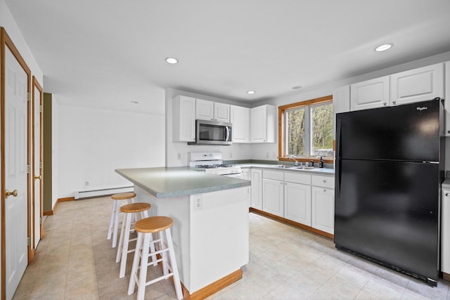 kitchen featuring freestanding refrigerator, stainless steel microwave, white range with gas stovetop, a baseboard heating unit, and white cabinetry