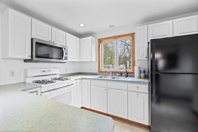 kitchen with freestanding refrigerator, stainless steel microwave, white gas range, a sink, and white cabinetry