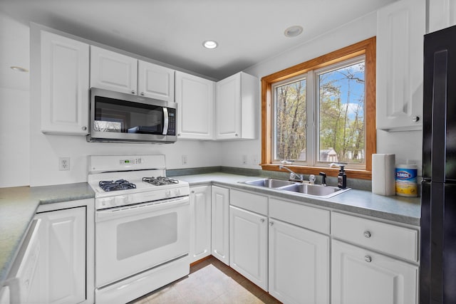 kitchen featuring stainless steel microwave, gas range gas stove, a sink, freestanding refrigerator, and white cabinetry