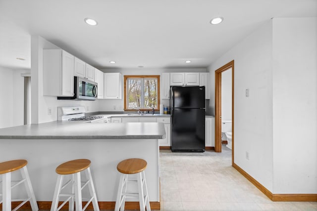 kitchen with freestanding refrigerator, stainless steel microwave, white gas range oven, a peninsula, and a kitchen bar