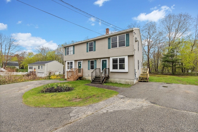 colonial home with asphalt driveway, a chimney, and a front lawn
