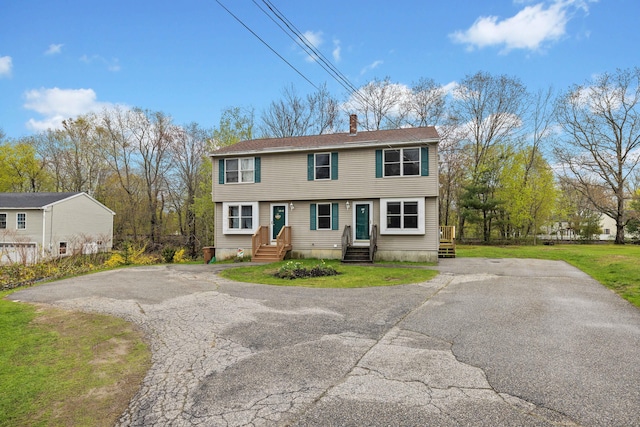 colonial house with a chimney, driveway, entry steps, and a front yard