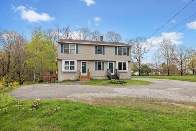 colonial house with entry steps, a chimney, driveway, and a front yard