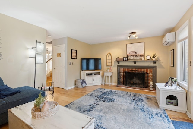 living room featuring a wall unit AC, light wood-style flooring, a fireplace, stairs, and baseboards
