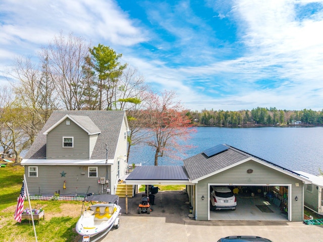 view of front of house with a carport, driveway, a water view, a garage, and roof mounted solar panels