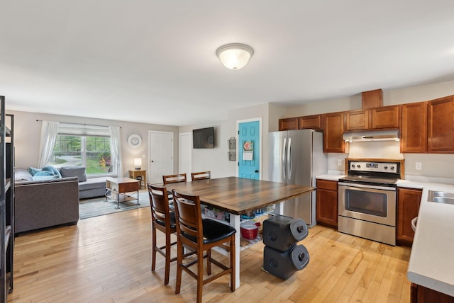 kitchen with stainless steel appliances, light wood finished floors, light countertops, open floor plan, and under cabinet range hood
