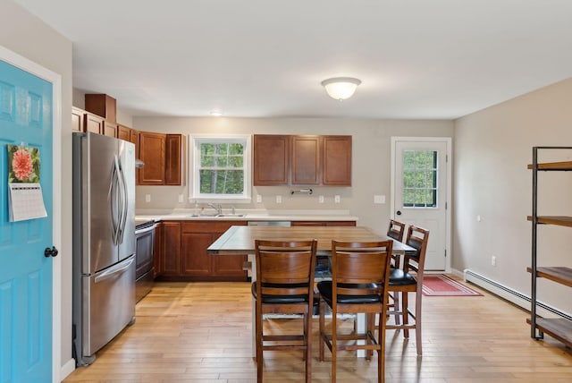kitchen with stainless steel appliances, a sink, light countertops, light wood finished floors, and a baseboard radiator