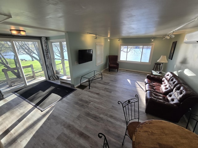 living area featuring rail lighting, a wall mounted AC, baseboards, and wood finished floors