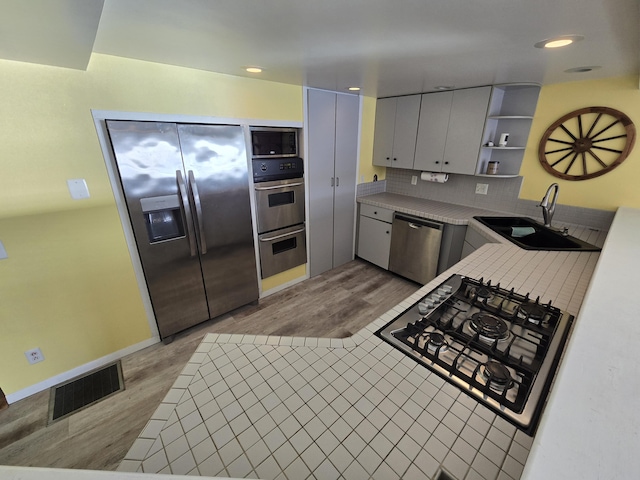 kitchen with visible vents, a sink, open shelves, stainless steel appliances, and light wood-type flooring
