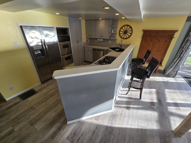 kitchen featuring a sink, stainless steel appliances, wood finished floors, open shelves, and visible vents