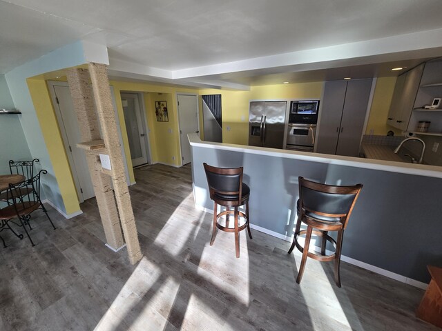 kitchen featuring a sink, wood finished floors, a breakfast bar, baseboards, and appliances with stainless steel finishes