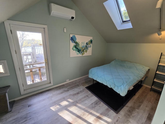 bedroom with a wall mounted AC, baseboards, lofted ceiling with skylight, and wood finished floors