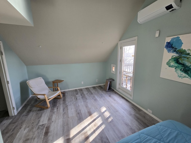 interior space with baseboards, a wall mounted air conditioner, wood finished floors, and vaulted ceiling