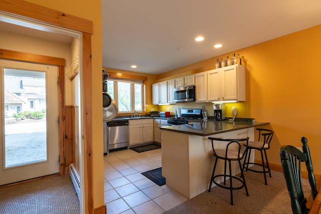 kitchen featuring a peninsula, a sink, dark countertops, baseboard heating, and appliances with stainless steel finishes