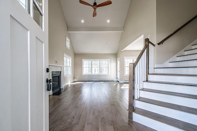 unfurnished living room with a towering ceiling, a ceiling fan, baseboards, stairway, and a glass covered fireplace