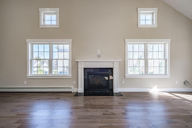 unfurnished living room featuring a towering ceiling, baseboard heating, wood finished floors, and a fireplace with flush hearth