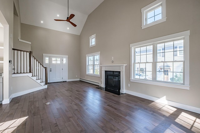 unfurnished living room featuring baseboard heating, high vaulted ceiling, a ceiling fan, dark wood finished floors, and stairs