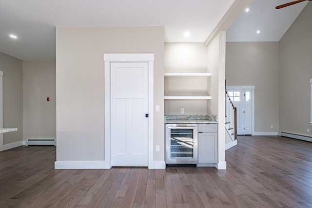 kitchen with beverage cooler, dark wood finished floors, a baseboard heating unit, a ceiling fan, and baseboards