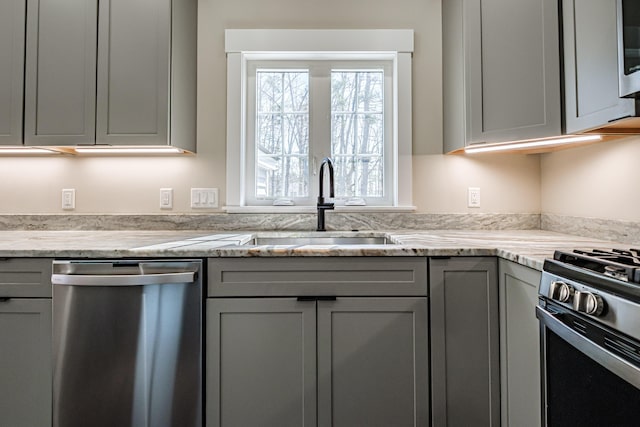 kitchen featuring stainless steel dishwasher, a sink, gray cabinetry, light stone countertops, and range with gas stovetop