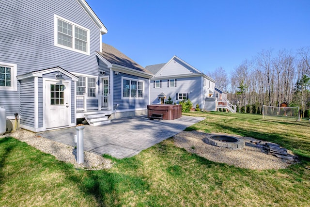 rear view of property with a hot tub, an outdoor fire pit, a patio area, and a lawn