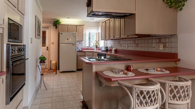 kitchen with freestanding refrigerator, black oven, stainless steel microwave, a peninsula, and tasteful backsplash