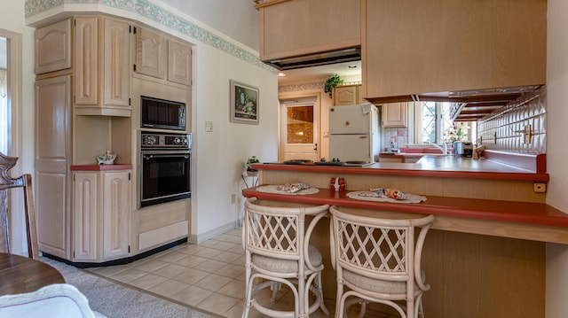kitchen with black appliances, light tile patterned floors, a breakfast bar area, a peninsula, and baseboards