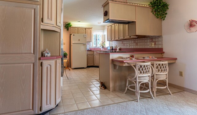 kitchen featuring freestanding refrigerator, a peninsula, a breakfast bar area, light brown cabinetry, and tasteful backsplash