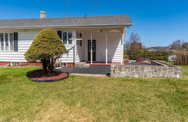 back of property featuring a yard, a chimney, and roof with shingles