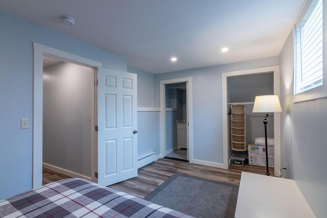 unfurnished bedroom with wood finished floors, a closet, a walk in closet, baseboards, and baseboard heating