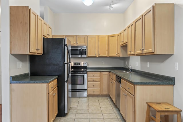 kitchen featuring appliances with stainless steel finishes, a sink, dark countertops, and light brown cabinets