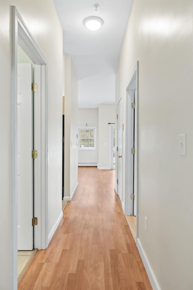 hall featuring light wood finished floors, a baseboard heating unit, and baseboards