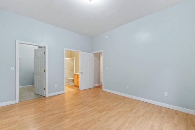 unfurnished bedroom with baseboards, light wood-style floors, a spacious closet, and ensuite bathroom