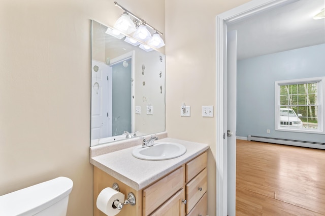 bathroom with toilet, vanity, a baseboard heating unit, and wood finished floors