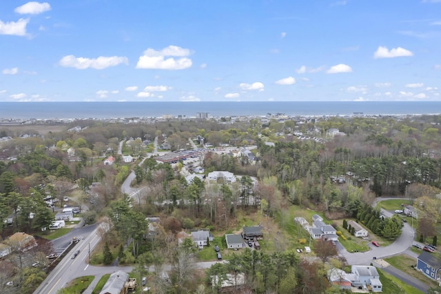 aerial view of property and surrounding area featuring a nearby body of water, a tree filled landscape, and nearby suburban area
