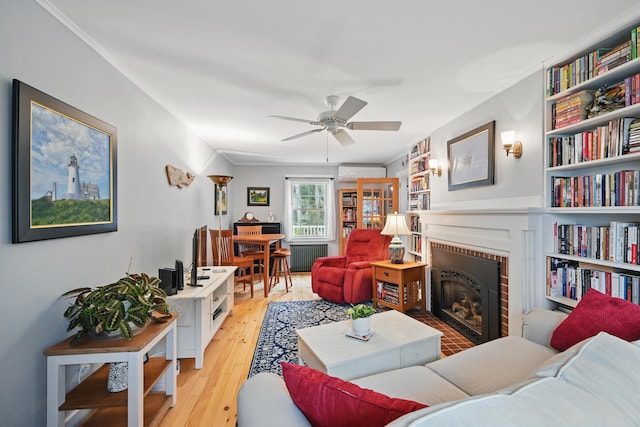 51 Googin St, Lewiston, ME 04240 - living area with radiator, a wall unit AC, a brick fireplace, ceiling fan, and hardwood / wood-style flooring