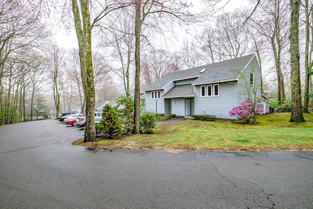 view of front of home with a shingled roof, a front lawn, and uncovered parking