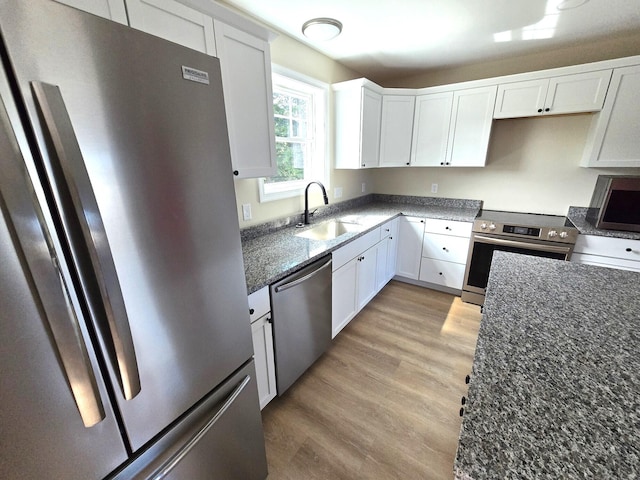 kitchen featuring dark stone countertops, a sink, stainless steel appliances, light wood-type flooring, and white cabinetry