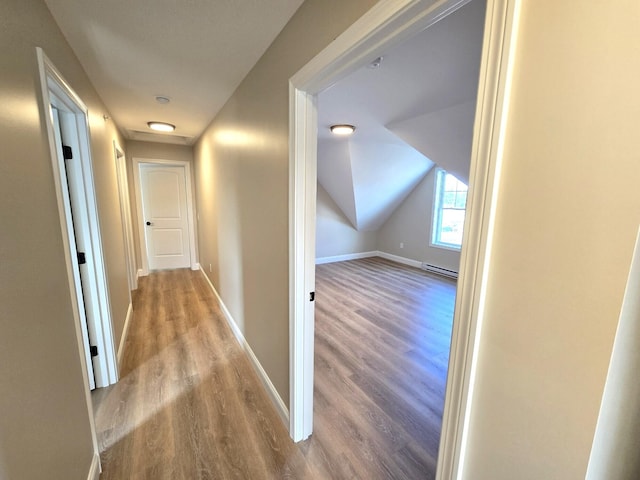 hall featuring lofted ceiling, a baseboard heating unit, baseboards, and wood finished floors