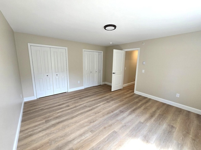 unfurnished bedroom featuring baseboards, light wood-style floors, and multiple closets