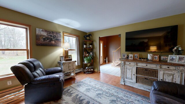 living room with plenty of natural light, stairs, light wood-type flooring, and a baseboard heating unit
