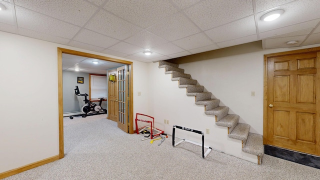 finished below grade area featuring carpet floors, stairs, a drop ceiling, and baseboards