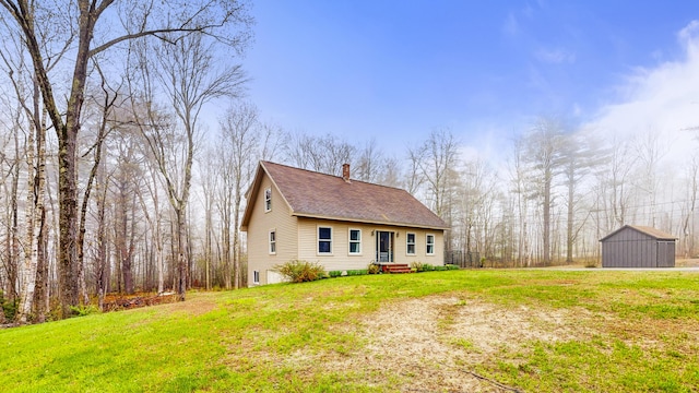 view of front facade featuring a chimney, a front lawn, a shed, an outbuilding, and roof with shingles