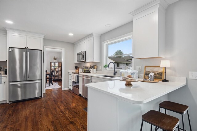 kitchen with appliances with stainless steel finishes, a sink, white cabinets, a kitchen bar, and recessed lighting
