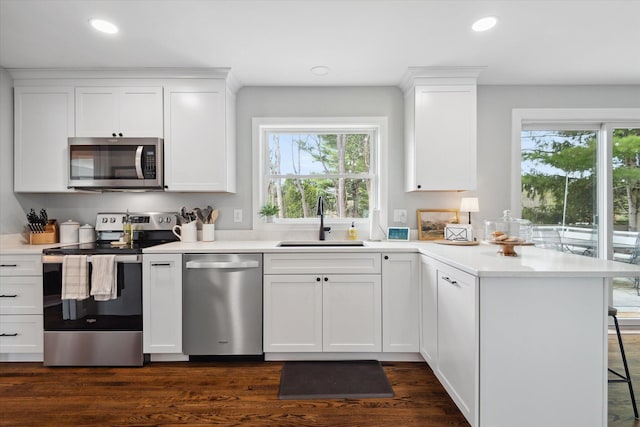 kitchen with appliances with stainless steel finishes, a sink, a peninsula, white cabinetry, and light countertops