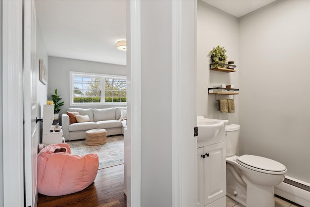 half bath featuring baseboard heating, toilet, vanity, and wood finished floors