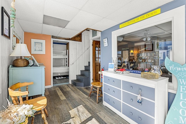 below grade area with wood finished floors, a drop ceiling, ceiling fan, and stairway