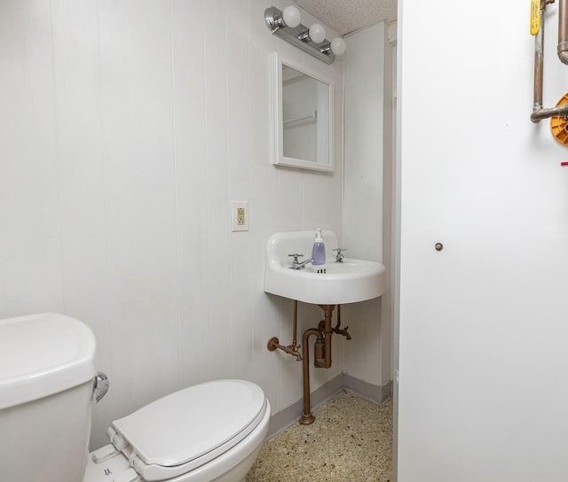 bathroom with speckled floor, toilet, baseboards, and a sink