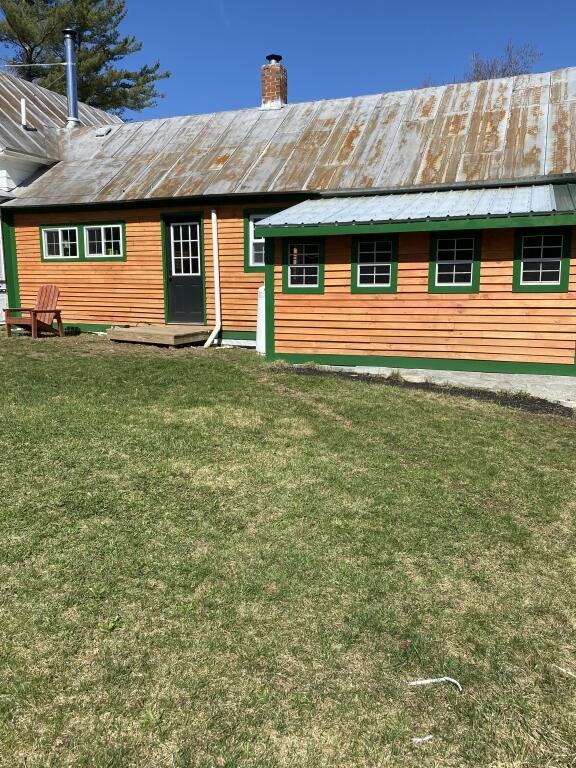 back of property with metal roof, a lawn, and a chimney