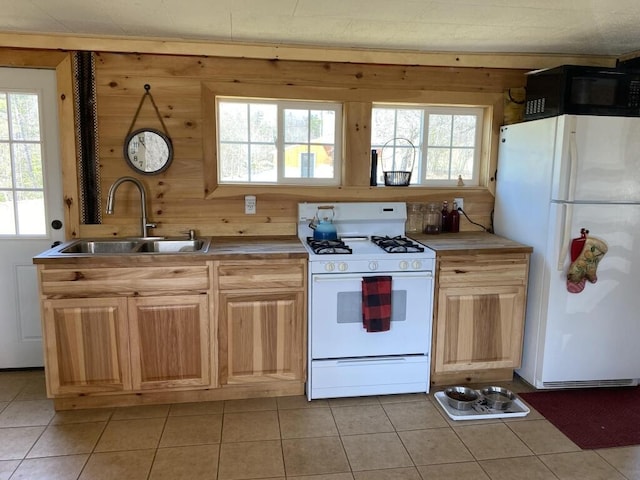 kitchen featuring white appliances, a sink, light tile patterned floors, plenty of natural light, and wood walls