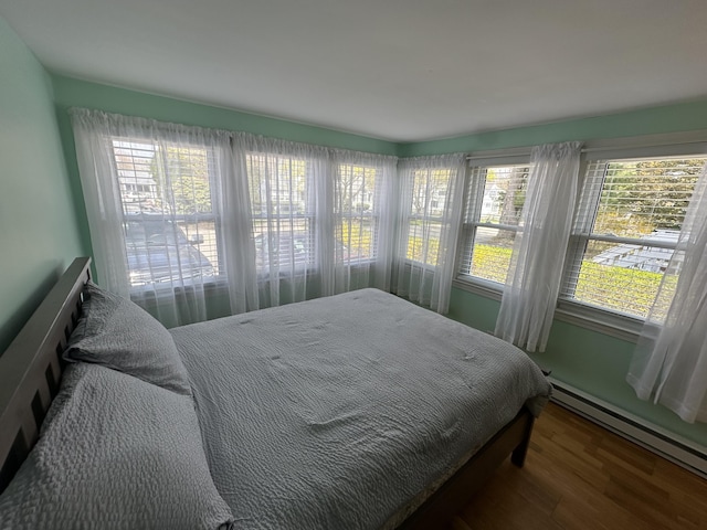 bedroom with wood finished floors and a baseboard heating unit